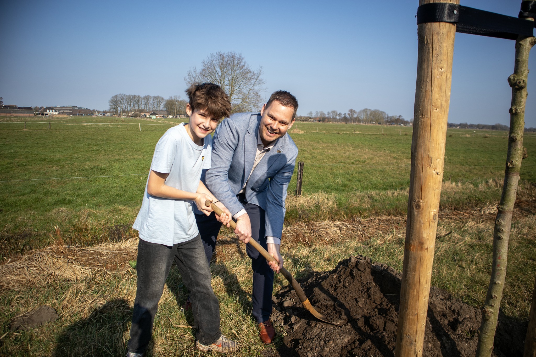 Een leerling van PCBS De Borchstee plant samen met wethouder Lennart Oosterloo een boom tijdens de Boomplantdag