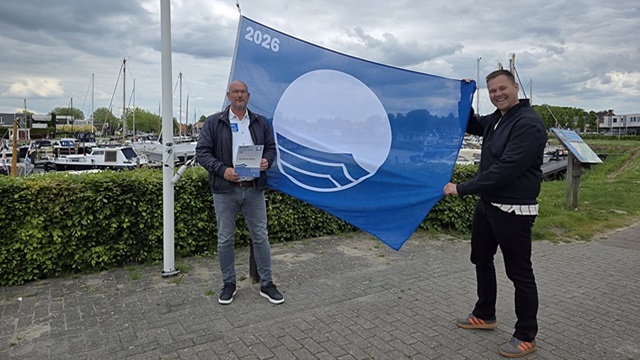 Wethouder Lennart Oosterloo en havenmeester Henk Kroes nemen de blauwe vlag in ontvangst tijdens de landelijke uitreiking in Hoorn