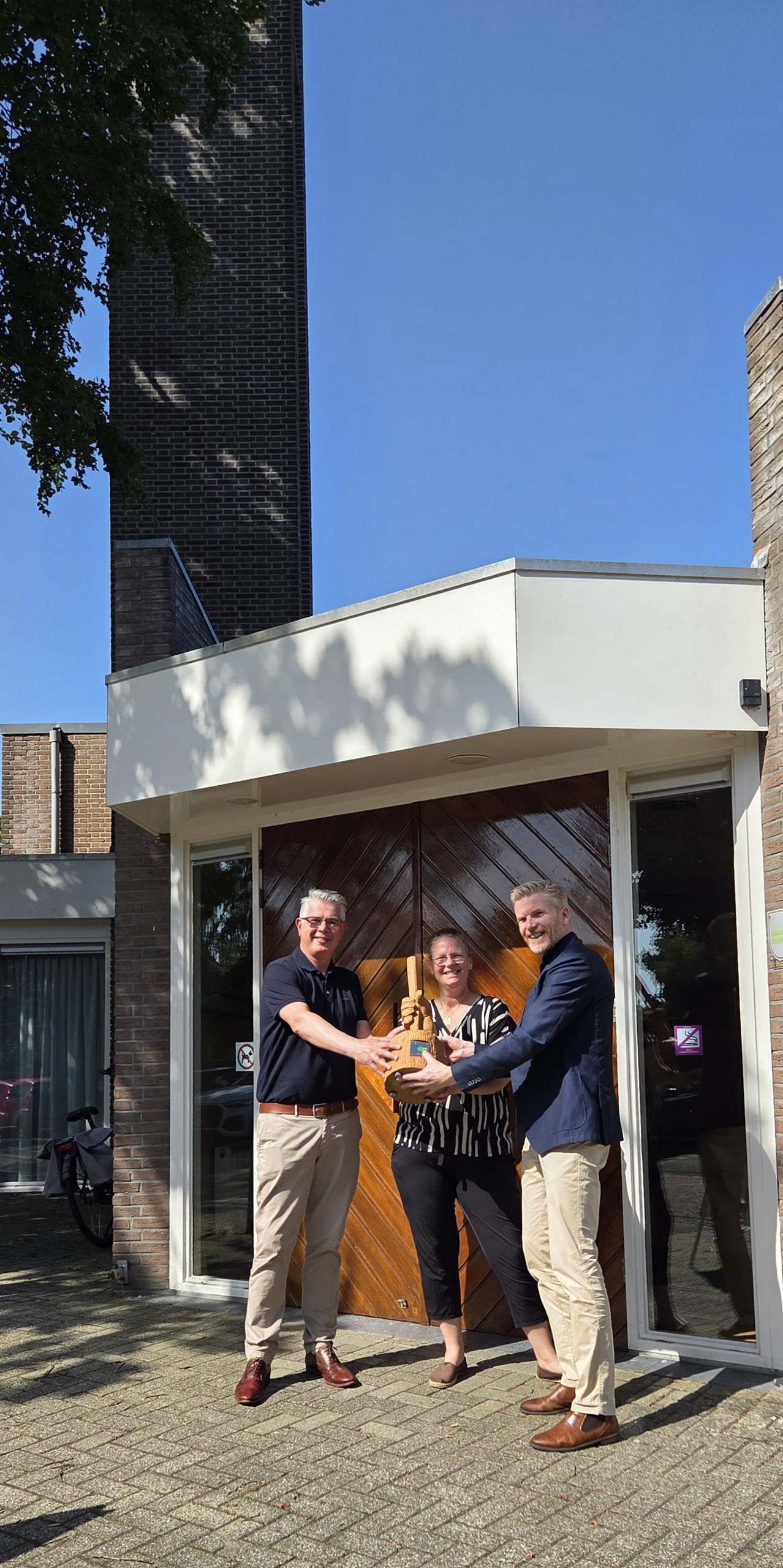 Wethouder Lambert Polinder, reikt de Klimaatestafette uit aan Aart van Putten, voorzitter van het College van Kerkrentmeesters en Manon Sluijter, voorzitter van de kerkenraad